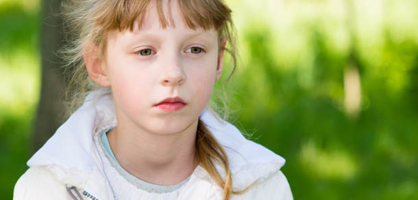 Teenage girl in wooded area, wearing warm clothes, looking sad