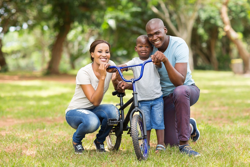 a foster child riding a bike in the park with his foster parents